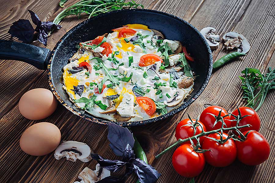 Fried eggs on a pan served with tomato, mushrooms, cheese, basil, onions and arugula.