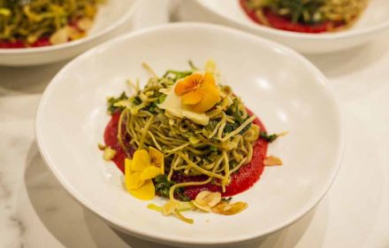 Chef Valeria Boselli presenting Vegan edamame pasta with edible flowers, toasted almonds, beetroot puree