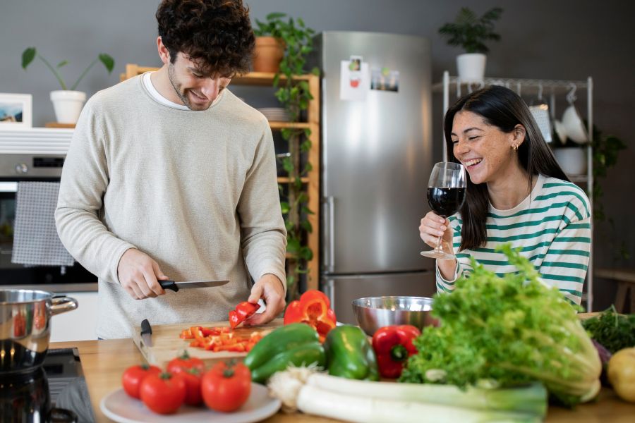 a couple cooking together while drinking wine