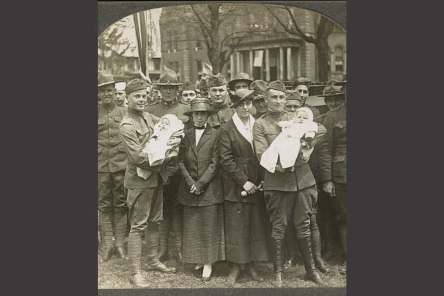 Historic black-and-white photo of soldiers holding babies beside their families
