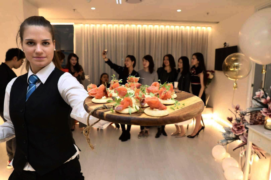 a waitress holding a platter of canapes in front of guests taking selfies